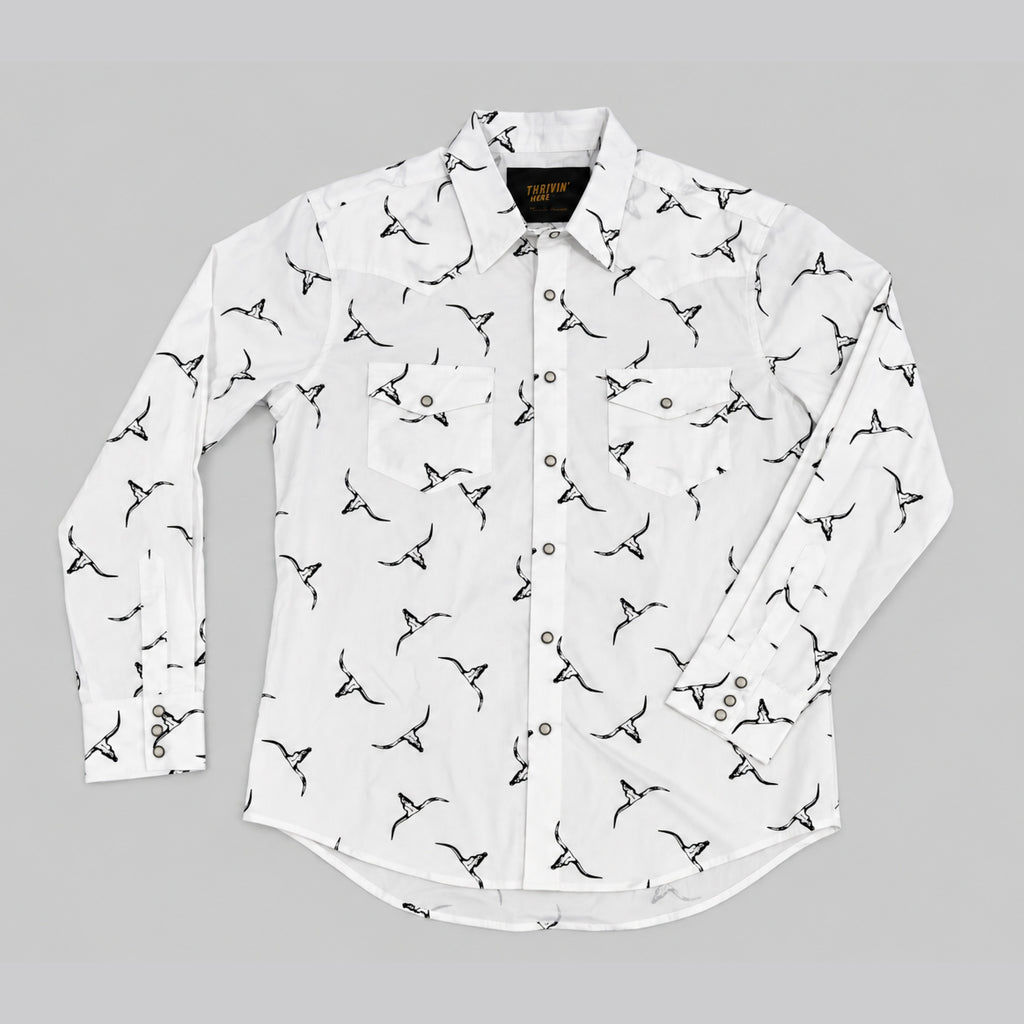 A white long-sleeve button-up shirt with an all-over black bird print, laid flat on a neutral gray background.