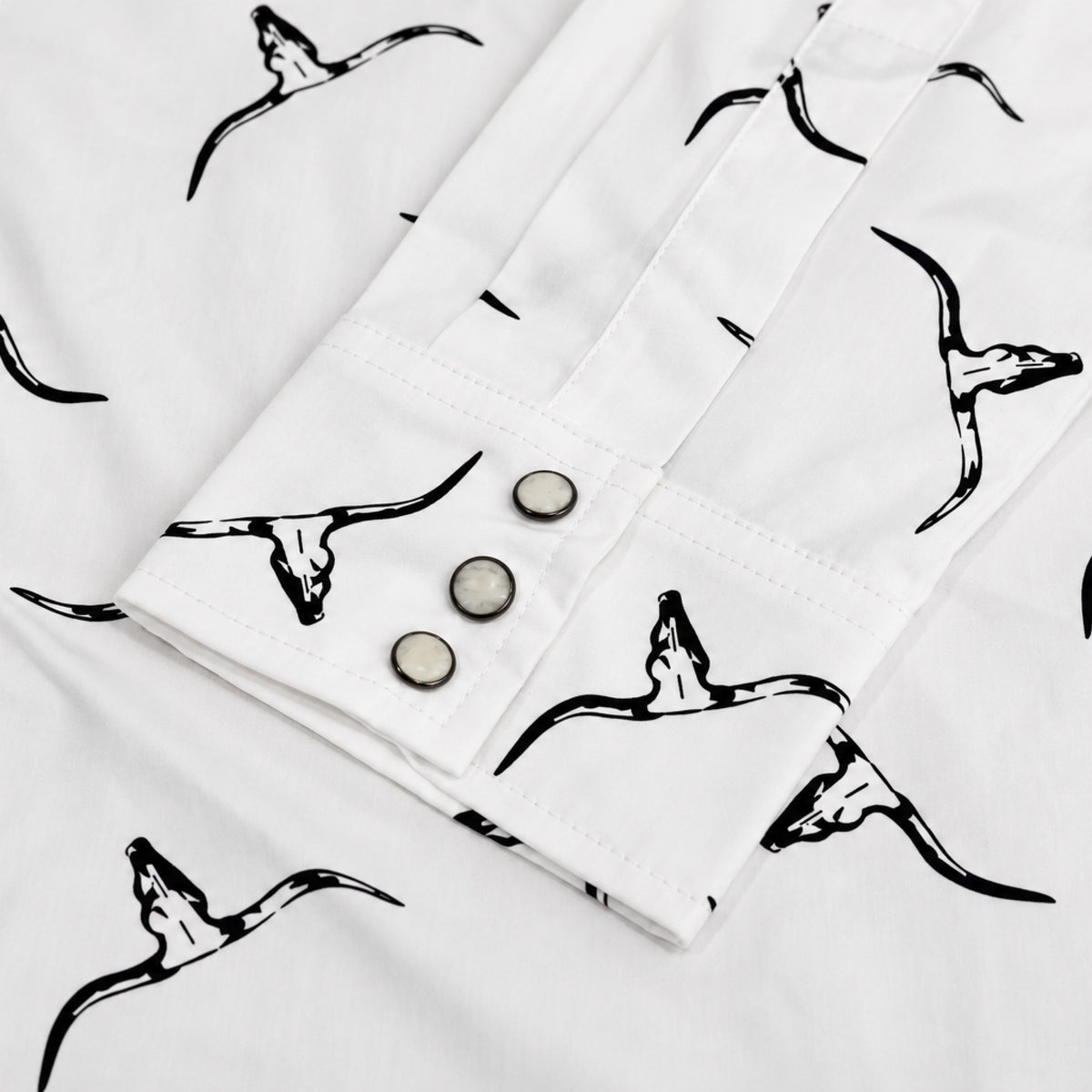 Close-up of a white shirt or jacket sleeve with a black longhorn/cow skull print and three metal buttons on the cuff.